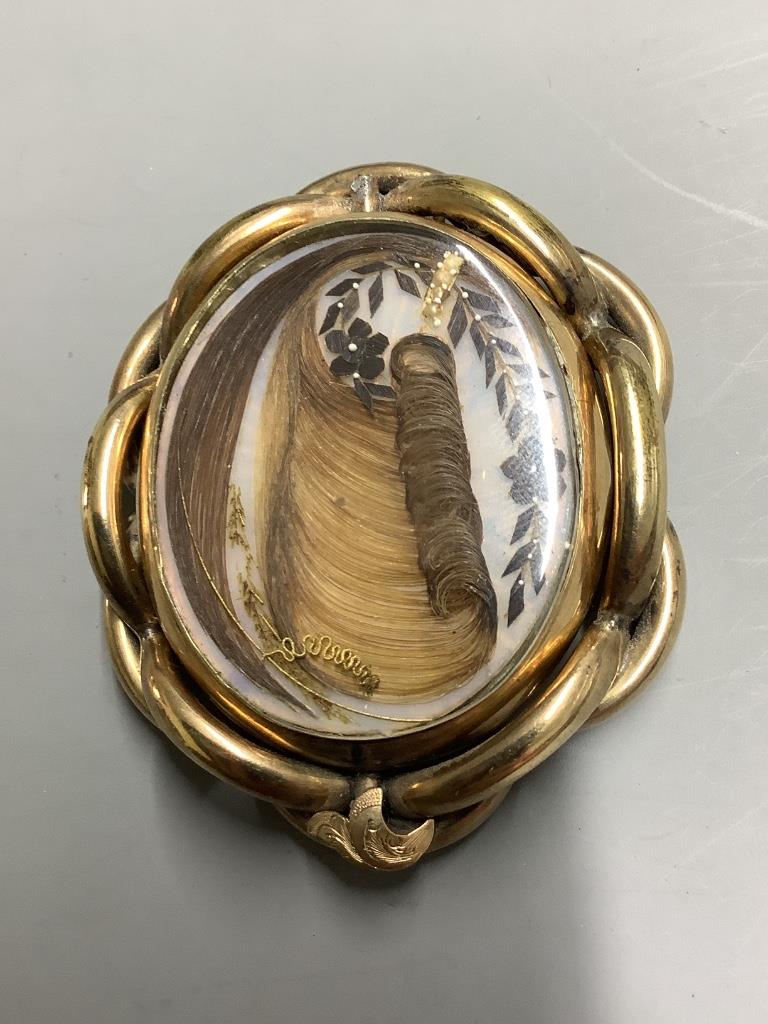 A Victorian pinchbeck and enamel revolving oval mourning pendant brooch, with plaited hair below a glazed panel, 64mm.